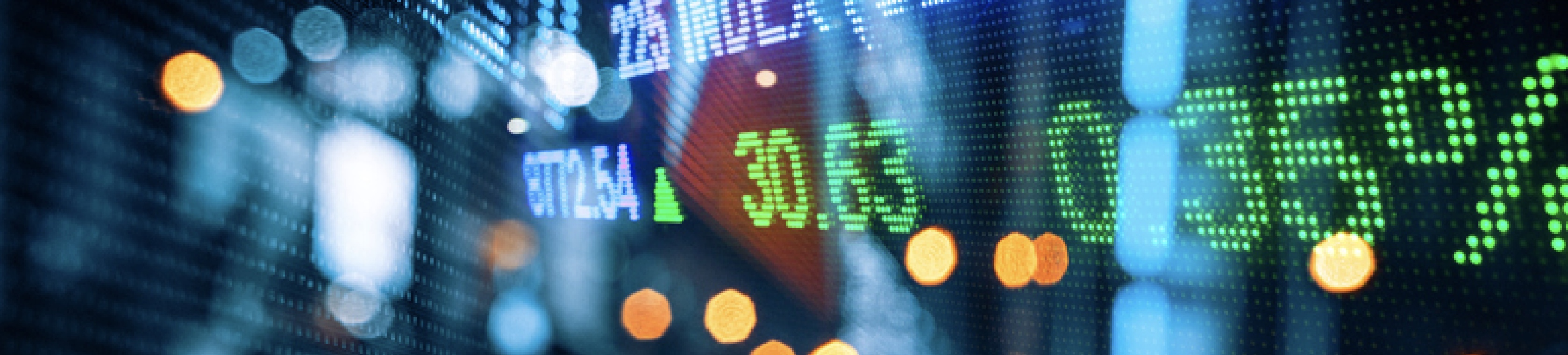 Close-up of a digital stock market display board showing green and blue numbers with bokeh lights, symbolizing financial data and trading activity.