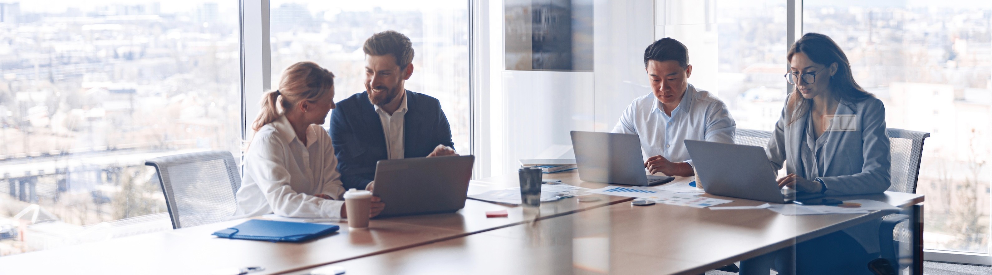 A group of professionals sitting at a table with laptops, engaged in a meeting.